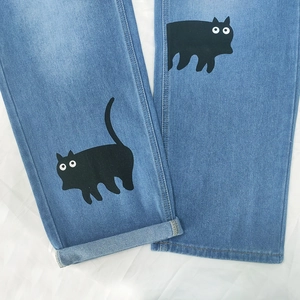 Détail d'un jean droit bleu clair avec un motif de chat noir imprimé sur la jambe