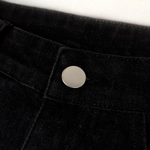 Detailed close-up of a black denim waistband featuring a minimalist silver metal button