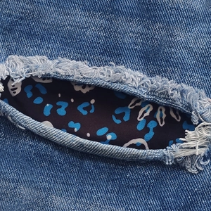 Detailed macro view of denim shorts with ripped edges and leopard print fabric patch