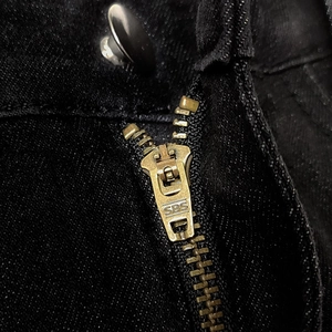 Detailed macro shot of a premium SBS metal zipper and black button on denim trousers