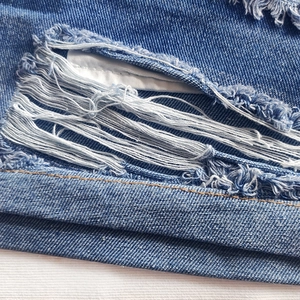 Close-up of distressed blue denim fabric with fringe detail and white pocket lining