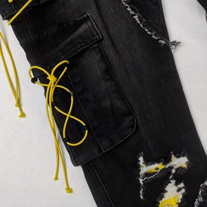 Detail of black cargo jeans featuring side pockets and yellow drawstring accents