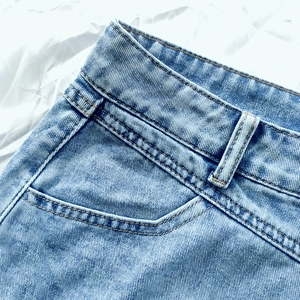 Detail of light blue denim skirt showing waistline, belt loops, and neat stitching accents
