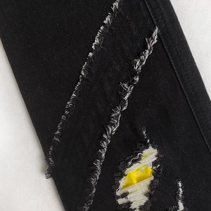 Macro shot of black denim distressed details with frayed edges and yellow contrast patch