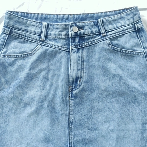 Detail shot of light blue denim skirt featuring waist loops and high-quality metal buttons