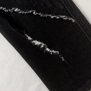 Close-up of black distressed denim fabric with ripped details and white frayed cotton edges