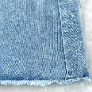 Detailed close-up of light blue denim skirt hem featuring casual raw fringe edges