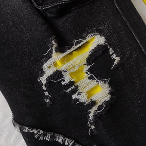 Black distressed denim pants featuring bold yellow lining detail and frayed ripped edges