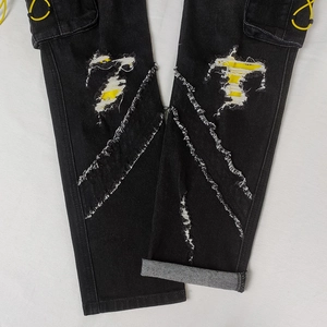 Detailed close-up of distressed black cargo jeans with yellow patchwork and drawstring pocket