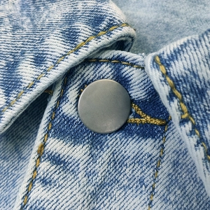 Macro detail of light blue denim fabric with silver button and yellow contrast stitching