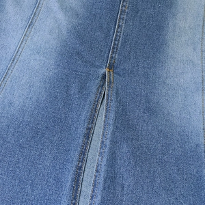 Close-up of light blue denim fabric texture with yellow stitching and slit detail
