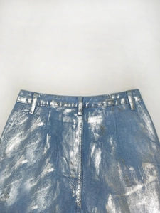 Détail d'un jean bleu avec des éclaboussures de peinture métallique argentée et des passants
