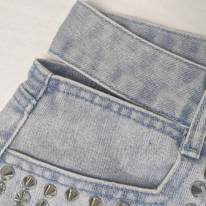Dettaglio macro del tessuto denim azzurro con borchie coniche in metallo argento
