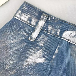 Détail du revêtement argenté sur jean bleu clair avec passants de ceinture et coutures