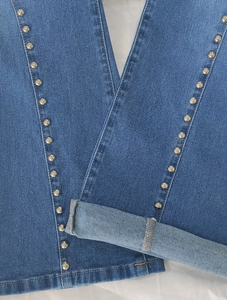 Detail of blue flare jeans with vertical silver metal rivets and cuffed hem finishing