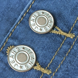 Detailed macro view of denim fabric with metallic jeans buttons and golden contrast stitching