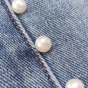 Dettaglio del tessuto denim blu con perle bianche incastonate e cuciture marrone dorato