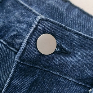 Macro view of a matte silver metal button on dark indigo twill denim high-waisted jeans