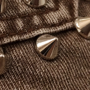 Detailansicht der silbernen Metallnieten auf braunem Denim-Stoff der Jacke