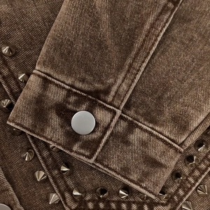 Detailaufnahme der braunen Jeansjacke mit metallischen Nieten und silbernem Knopf am Ärmel