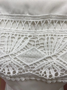 Macro view of white geometric lace stitching on off-shoulder fashion dress fabric