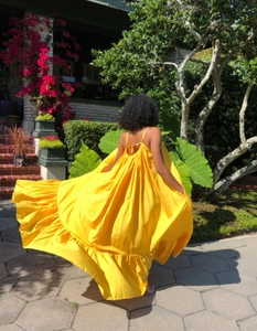 Detail of a bright yellow sleeveless maxi dress with thin straps and ruffled hemline