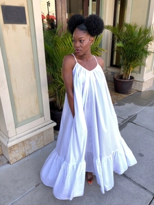 Detail view of flowy white spaghetti strap maxi dress with ruffled hem in tropical setting