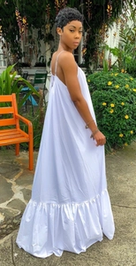 Detailed view of white spaghetti strap dress with ruffled hem in an outdoor garden setting