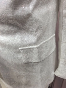 Close-up of white sequined blazer fabric featuring a flap pocket and shimmering details