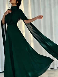 Detail of emerald green high-neck dress with long flowing chiffon cape sleeves and pleated waist