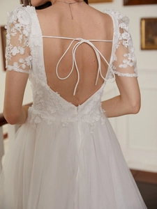 Detailed back view of white lace floral embroidery with delicate bow tie and open back dress