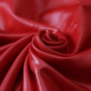 Detailed view of high-gloss red PU leather fabric with elegant spiral texture and drape