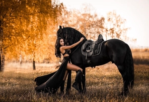 Detail of elegant black lace high slit dress paired with a black horse in a forest