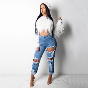 Detail view of white knit pullover with long fringe tassels and blue distressed denim jeans