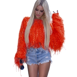 Détail d'un pull en peluche orange avec des paillettes dorées étincelantes et franges