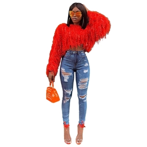 Détail d'un pull rouge à franges avec un jean bleu délavé et un sac à main orange