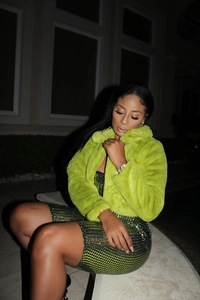 Detail of neon green faux fur jacket with wide collar and dark green sequined dress