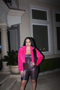 Detail of a bright pink faux fur jacket paired with a colorful sequined bodysuit for parties