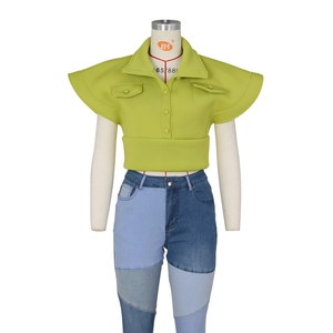Detail of green vest with flutter sleeves and asymmetrical patchwork denim jeans on mannequin