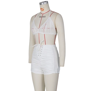 Detail of white crochet halter top and high-waisted pleated shorts with lace-up front