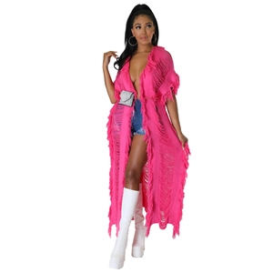 Détail du long cardigan en maille rose vif avec découpes et pompons à franges bohèmes