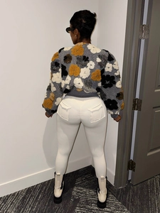 Detail view of the gray plush jacket featuring 3D floral accents and white tight trousers