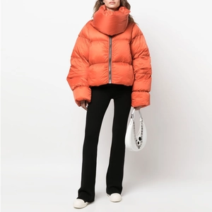 Detailed view of women's bright orange puffer jacket with high neck and sleek metal zipper