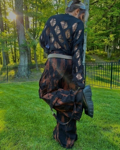 Back view of a street style black cutout knit sweater and tie-dye cargo pants with straps