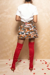 Détail d'une mini-jupe camouflage taille haute avec ourlet brut et étiquettes décoratives rouges