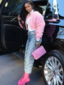 Chic pink faux fur jacket styled with blue jeans and high boots by a black SUV