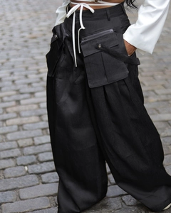 Detail of black cargo pants featuring textured fabric and oversized removable pocket design