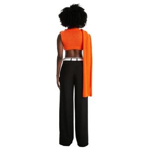 Vista posteriore del gilet in maglia arancione da donna con pantaloni neri larghi e sciarpa