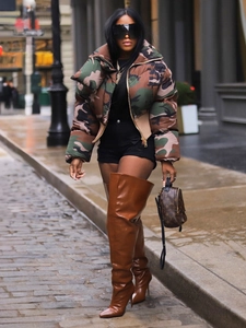 Chic women's cropped camo puffer jacket paired with high boots in a city street setting