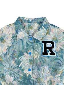 Detailed view of floral jacquard jacket featuring a blue snap button and embroidered R letter patch